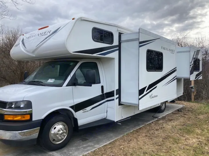 This white Coachmen Freelander Class C motorhome rv rental, with extended slide-outs, is parked on a concrete pad.. Coachmen 26DS 2021