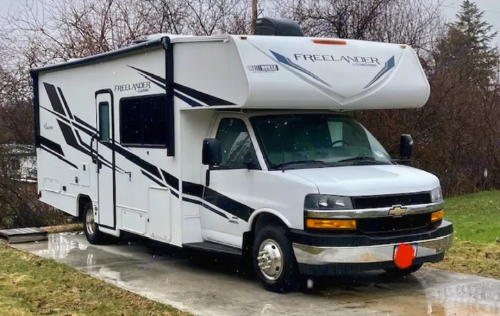 A white Coachmen Freeland Class C RV, ideal for an RV rental trip, is shown parked on a paved driveway.. Coachmen 26DS 2021