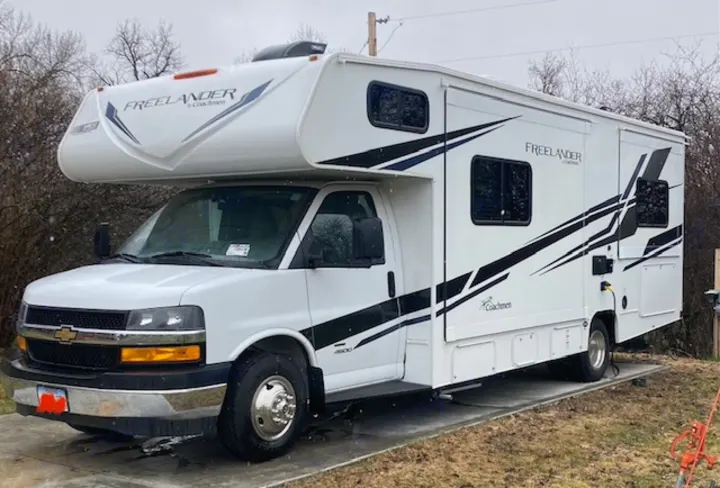 White Coachmen Freelander Class C RV rental, parked outdoors on concrete pads. Features black and blue graphic decals.. Coachmen 26DS 2021