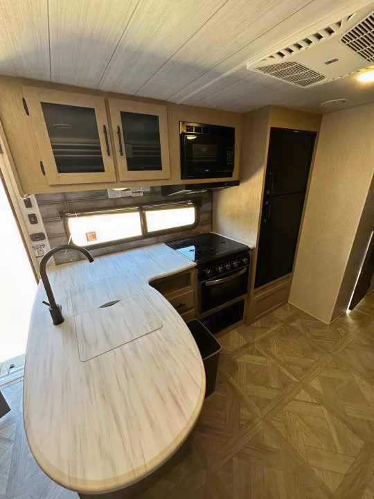 Modern RV rental kitchen with light wood cabinets, spacious counter, sink, stove, microwave, and fridge for comfortable travel.. Forest River Salem Cruise Lite T282QXBL 2023