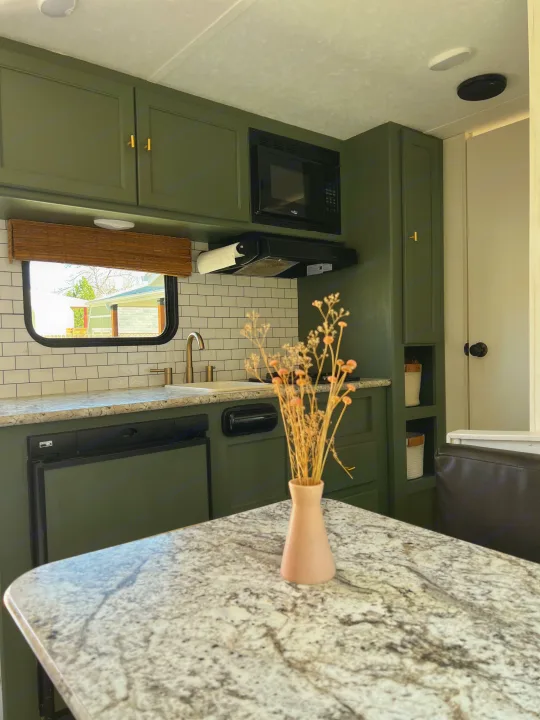 Inside an RV rental: Modern kitchen with olive green cabinets, subway tile backsplash, granite-look counters, and dried flowers.. Keystone RV Hideout 2018