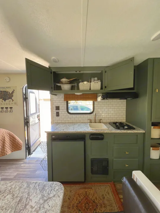 Modern green kitchen inside an RV rental, featuring subway tile, granite-patterned counters, sink, and stove.. Keystone RV Hideout 2018