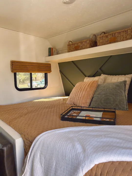 An inviting RV rental bedroom with a custom green headboard, storage shelf, and plush bedding.. Keystone RV Hideout 2018