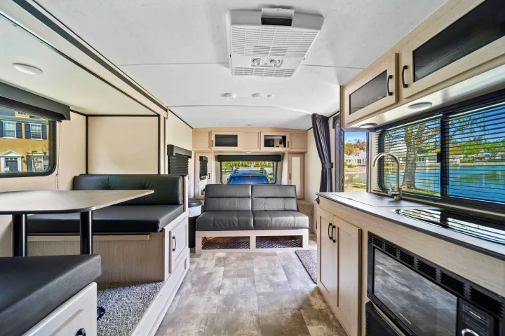 Bright rv rental interior, featuring a modern kitchen, dinette, and living area with couch, plus scenic window views.. Coachmen Apex 2022