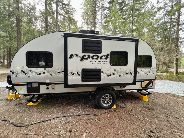 RV rental: A sleek r-pod travel trailer with honeycomb graphics is set up at a rustic forest campsite, nestled among trees.. Forest River R-Pod RP-190 2021