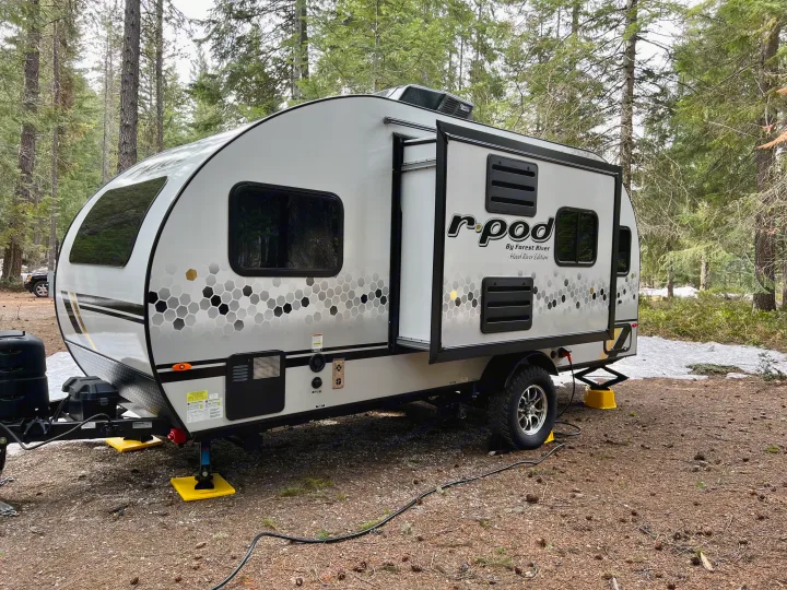 RV rental: r-pod travel trailer parked in a forest campsite, set up with leveling jacks on dirt and snow patches.. Forest River R-Pod RP-190 2021