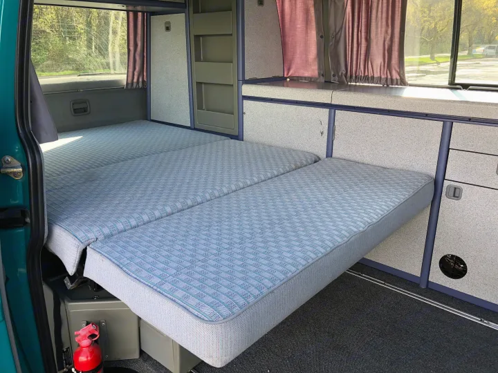 RV rental: Camper van interior shows convertible bed, cabinets & curtains. A ready-to-sleep travel setup.. Volkswagen T4 Westfalia Coach 1992