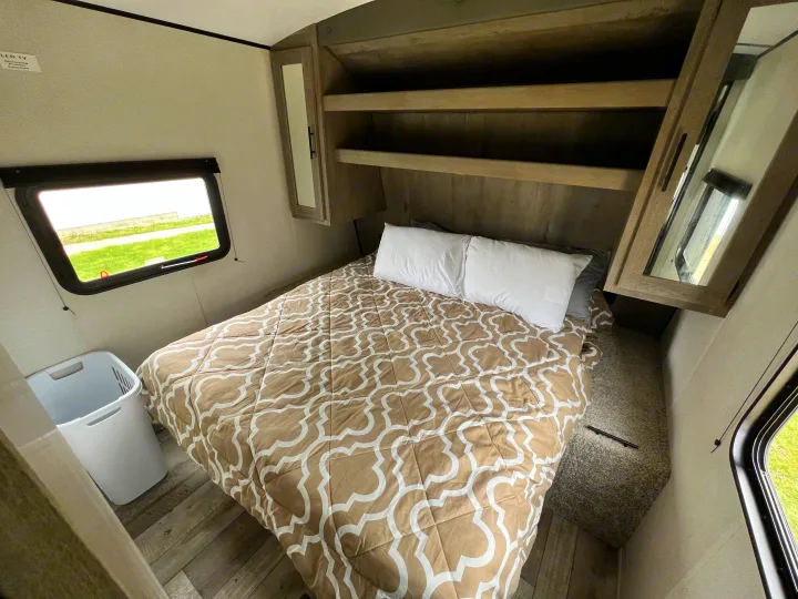 This RV rental bedroom offers a comfortable bed, overhead storage, mirrored cabinets, and a window with an outdoor view.. Keystone Springdale 2021