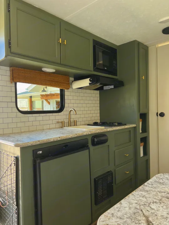 An olive green RV rental kitchen with subway tile backsplash, light countertops, and gold fixtures. Features microwave, stove, and fridge.. Keystone RV Hideout 2018