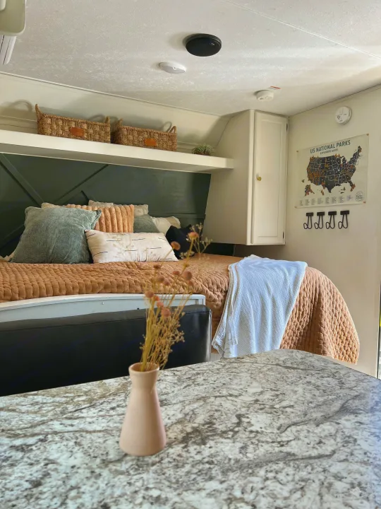 A cozy RV rental bedroom features a green headboard, map of US National Parks, and storage baskets, offering a comfortable stay.. Keystone RV Hideout 2018