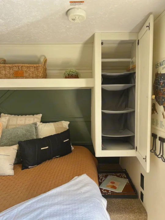 RV rental bedroom: cozy lower bunk with pillows, green wall, storage cabinet, and top shelf with basket. Compact comfort.. Keystone RV Hideout 2018