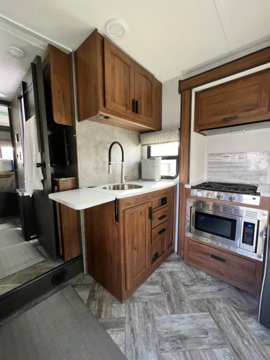 Clean RV rental kitchen: Sink, stove, microwave, wood cabinets, and sleek gray flooring visible.. Forest River Forester 2022