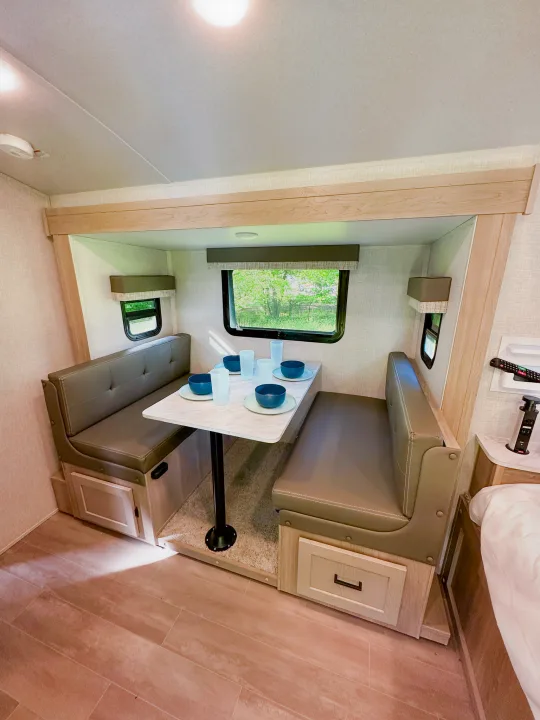 Inside an rv rental, a bright dinette area with booth seats, a table set with dishes, and windows to nature.. Forest River Flagstaff E-Pro 2023