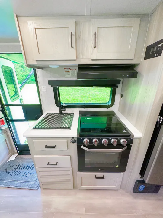 Bright RV rental kitchen with stove, oven, light cabinets, countertop, and window showing greenery.. Forest River Flagstaff E-Pro 2023