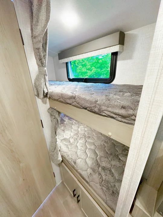 Cozy RV rental bunk beds with soft blankets and a window view of green trees.. Forest River Flagstaff E-Pro 2023