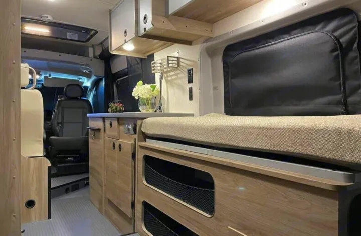 Inside a sleek **RV rental**: light wood cabinets, compact kitchen with a sink, and a comfortable bed. View of driver's cab.. Winnebago SOLIS 59 PX 2023