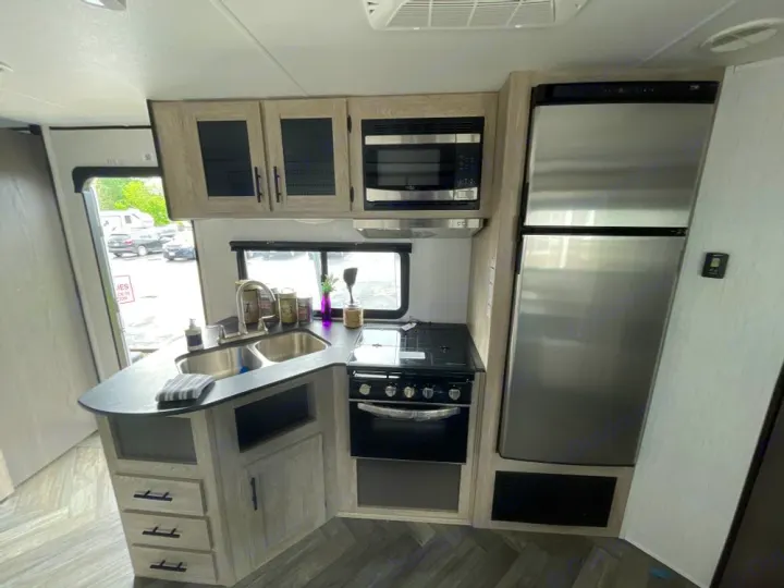 Modern RV rental kitchen interior featuring stainless steel appliances: fridge, stove, microwave, and double sink.. Heartland RVs Prowler 2022
