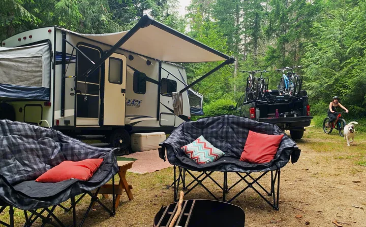 An RV rental provides comfort for a forest camping trip: travel trailer, cozy chairs, fire pit, and bikes for outdoor adventure.. Keystone RV Bullet Crossfire 2019
