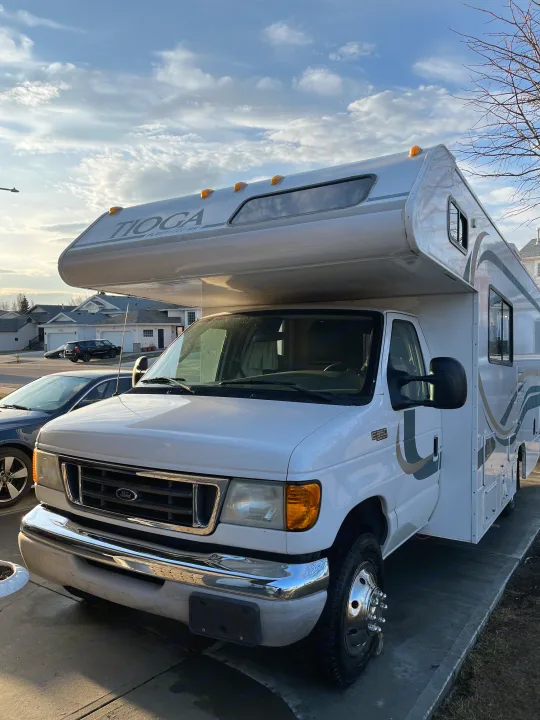 A white Ford Tioga Fleetwood Class C RV rental is parked on a sunny residential street.. Tioga Tioga Motorhome 2003