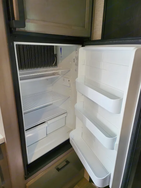 An empty, clean mini-fridge interior in an RV rental, showing shelves, door bins, and cooling fins.. Jayco Jay Feather Micro 2022