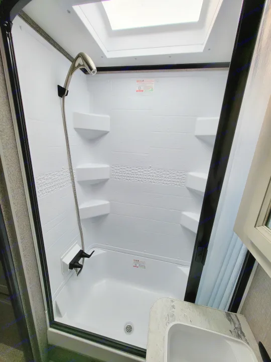 Bright white RV rental shower stall with textured walls, a showerhead, drain, and adjacent sink, ready for your travels.. Jayco Jay Feather Micro 2022