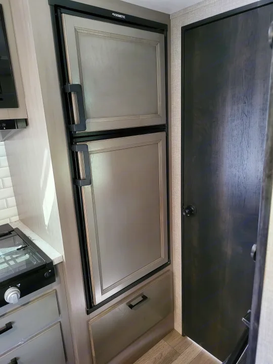 Inside an RV rental: View of the kitchen area with a dark wood overhead cabinet, Dometic refrigerator, and light-colored lower storage.. Jayco Jay Feather Micro 2022