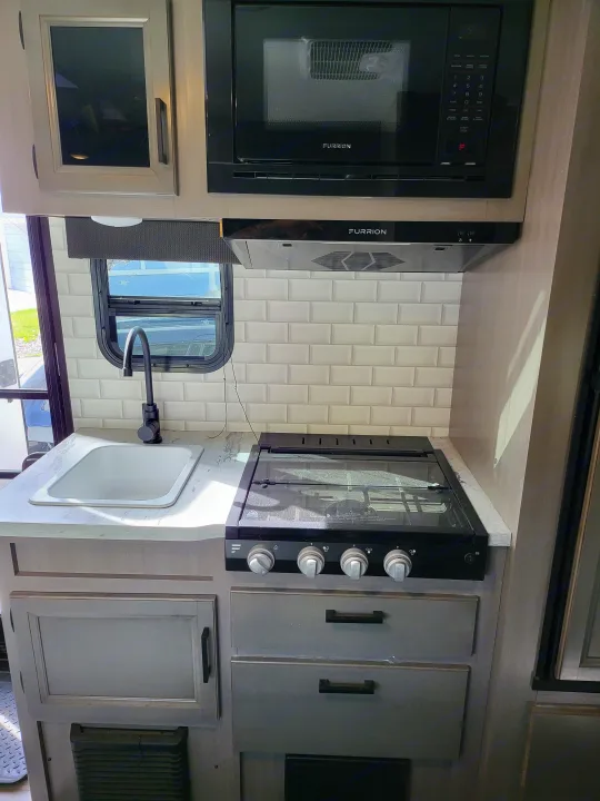 Modern RV rental kitchen with microwave, stove, sink, and cabinets, offering essential amenities for your travels.. Jayco Jay Feather Micro 2022