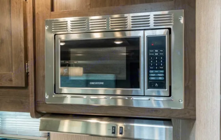 Stainless steel GREYSTONE microwave and range hood setup in a modern RV rental kitchen, with light and fan switches below.. Coachmen Pursuit 2022