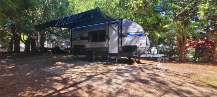 This modern RV rental travel trailer is parked at a shaded campsite, featuring an extended awning with blue LED lights.. Forest River Salem FSX 2022