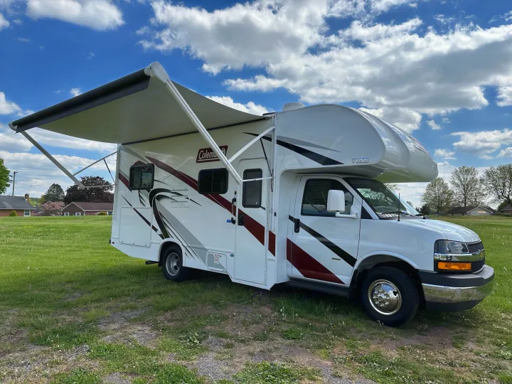 White Class C rv rental with awning extended, parked on grass under a sunny sky. Perfect for outdoor adventures.. Thor Coleman 2023