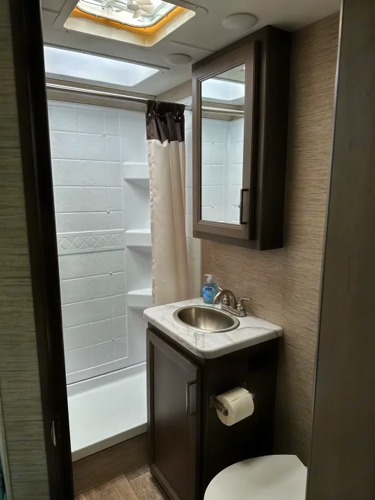 Modern RV rental bathroom with a marble-look counter, sink, mirror, toilet, and shower. Compact and functional space.. Thor Coleman 2023