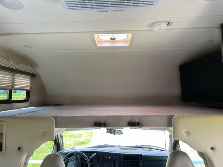 Spacious RV rental interior: overhead bunk, driver's area, and ceiling amenities including AC, skylight, and smoke detector.. Thor Coleman 2023