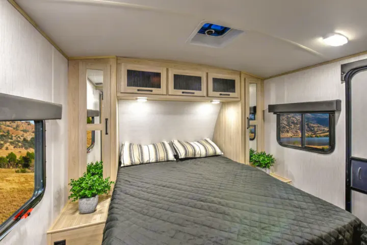 Cozy RV rental bedroom with a dark quilted bed, pillows, overhead storage, bright reading lights, and scenic window views.. Heartland RVs Sundance Ultra Lite 2022