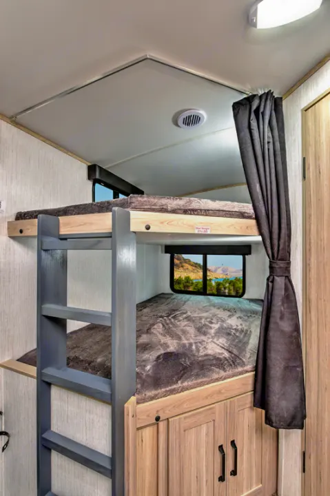 Detailed view of an **RV rental**'s interior with two stacked bunk beds, a ladder, and a window displaying a scenic outdoor landscape.. Heartland RVs Sundance Ultra Lite 2022