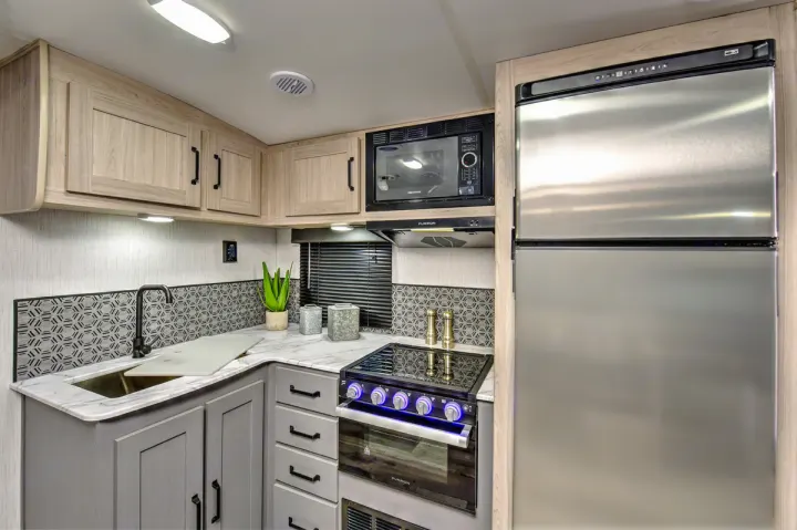 Modern RV kitchen with light wood & gray cabinets, stainless appliances, and unique backsplash, perfect for any rv rental.. Heartland RVs Sundance Ultra Lite 2022