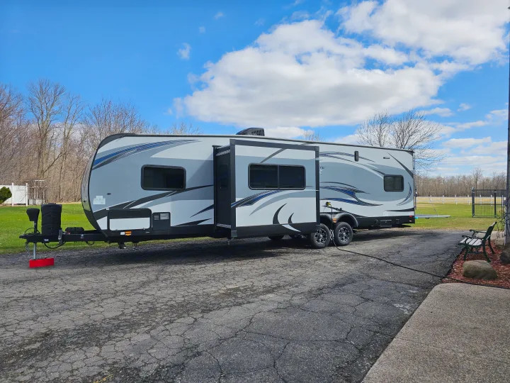 A large grey RV rental with blue graphics is parked on a driveway with its slide-out extended, ready for a trip.. Forest River XLR Hyperlite 30HDS 2017