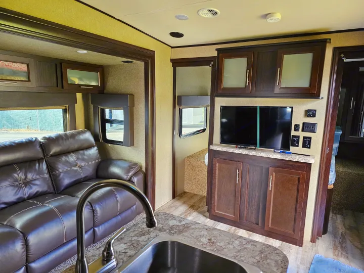 RV rental living area featuring a comfy leather sofa, well-equipped kitchenette with sink, TV, and dark wood cabinetry.. Forest River XLR Hyperlite 30HDS 2017