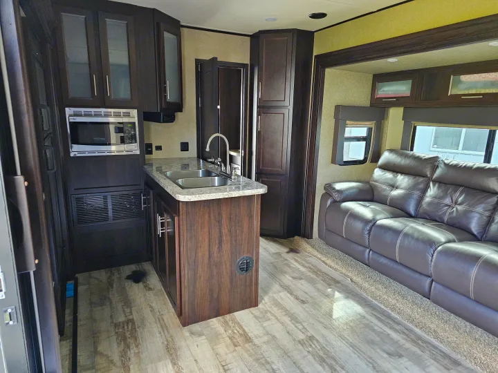 Modern RV rental interior with full kitchen, dark wood cabinets, and a comfortable living area featuring a brown leather sofa.. Forest River XLR Hyperlite 30HDS 2017