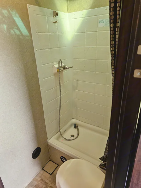 Compact RV rental bathroom: view of a white shower with textured walls, handheld showerhead, and part of the toilet.. Forest River XLR Hyperlite 30HDS 2017