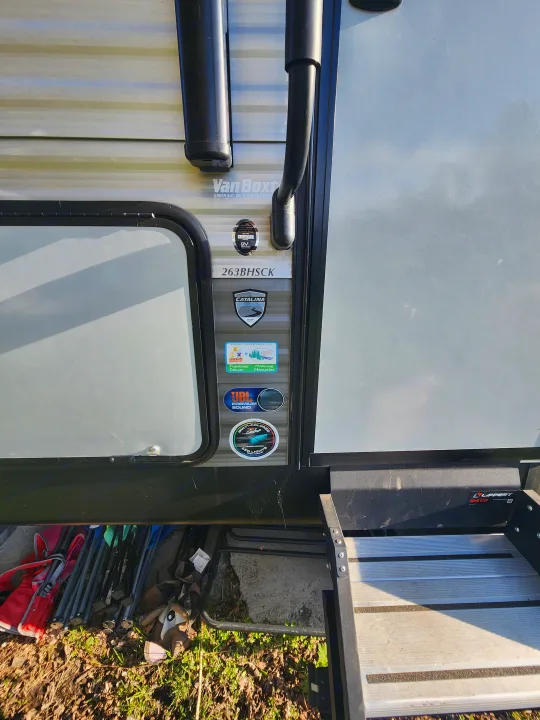 Side view of an RV rental, showing its open Lippert Solid Steps, entrance door, and various feature stickers.. Coachmen Catalina 263 bunk 2022