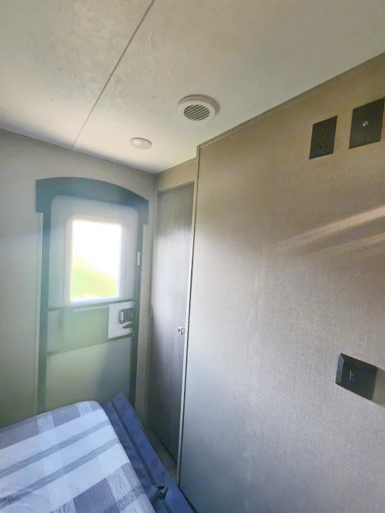 Inside an RV rental bedroom: looking up at the ceiling with power outlets, vent, and bright window above the bed.. Coachmen Catalina 263 bunk 2022