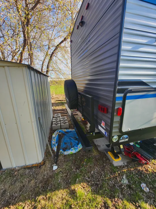 An RV rental is parked outdoors. Its side and rear are visible, showcasing a spare tire, lights, and stickers. A shed stands nearby.. Coachmen Catalina 263 bunk 2022