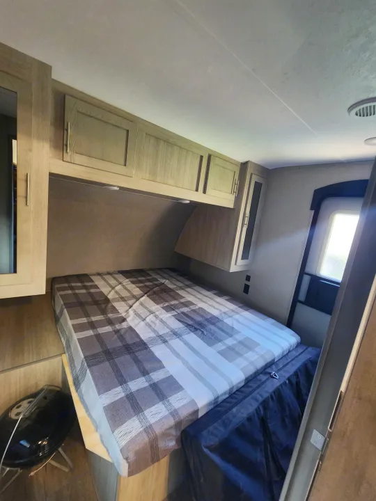 Cozy rv rental bedroom interior, featuring a bed with plaid comforter, wood cabinets, and a bright window.. Coachmen Catalina 263 bunk 2022
