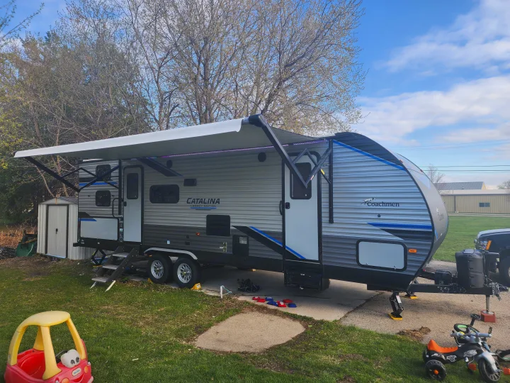 A modern Coachmen Catalina travel trailer, perfect for an rv rental, is set up with its extended awning and ready for outdoor fun.. Coachmen Catalina 263 bunk 2022