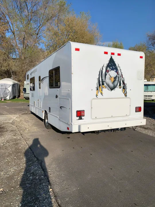 White RV rental with patriotic eagle decal parked at a sunny campground. Perfect for your next adventure.. Thor Majestic 2017