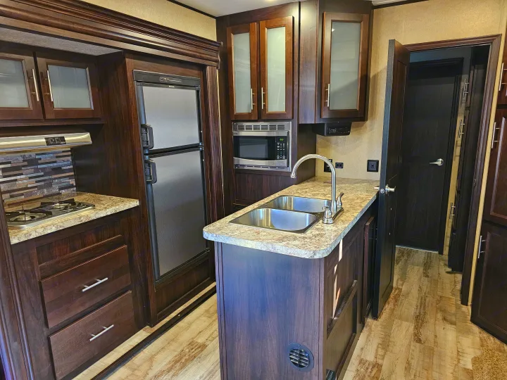 RV rental kitchen with dark wood cabinetry, double sink, stainless appliances (microwave, stove, fridge), and light countertops.. Forest River XLR Hyperlite 30HDS 2017