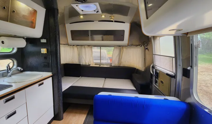 Inside this RV rental: compact kitchen, convertible sofa bed, and bright blue dining area, ready for adventure.. Airstream International 2004