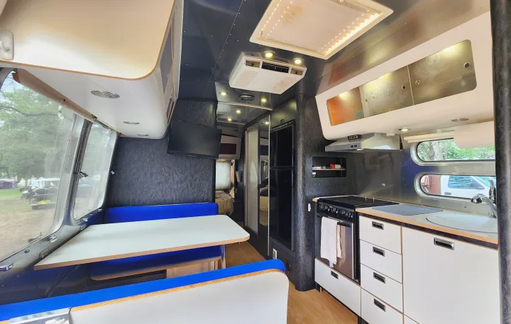 Spacious RV rental interior featuring a kitchen, dining area with blue benches, and rear bedroom.. Airstream International 2004
