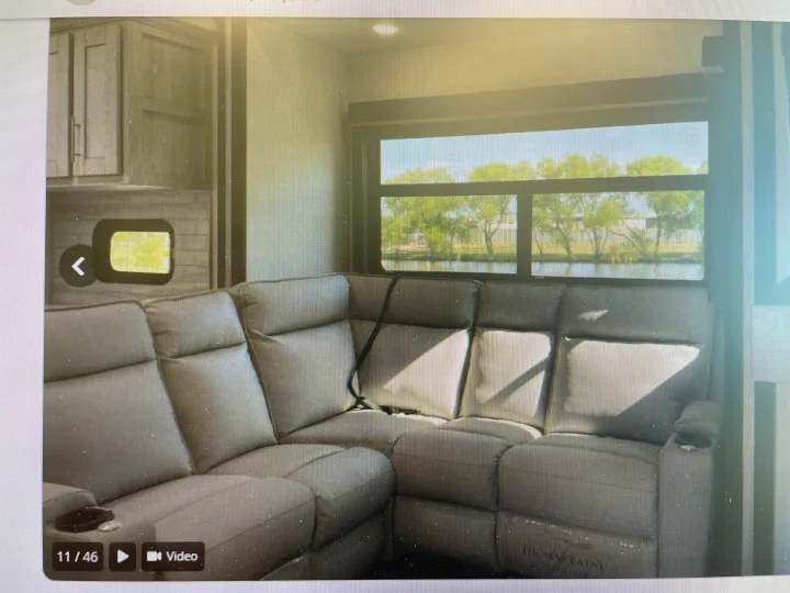 Spacious RV rental interior features a comfortable sectional sofa and a large window with scenic views of water and trees.. Keystone Fuzion 2021