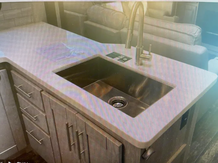 Modern RV rental kitchen with deep stainless steel sink, pull-down faucet, and sleek cabinets for comfortable travel.. Keystone Fuzion 2021